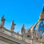 Vatican City statues and dome against blue sky.